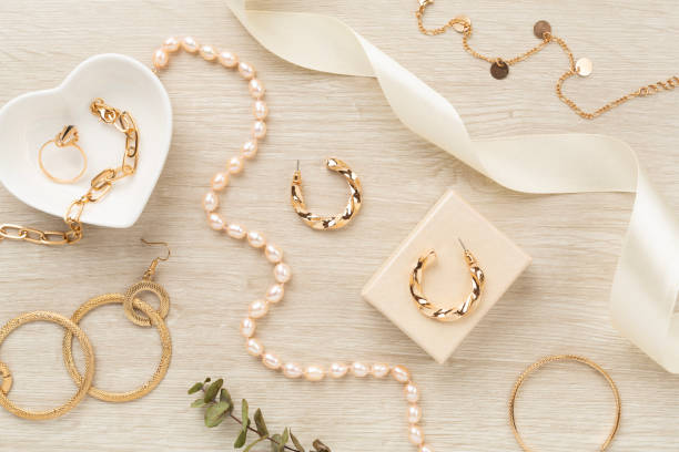 Vue de dessus élégante d'une collection de bijoux dorés et de perles sur un fond en bois clair, avec des boucles d'oreilles créoles torsadées, un collier de perles, une boîte cadeau et un ruban de satin.
